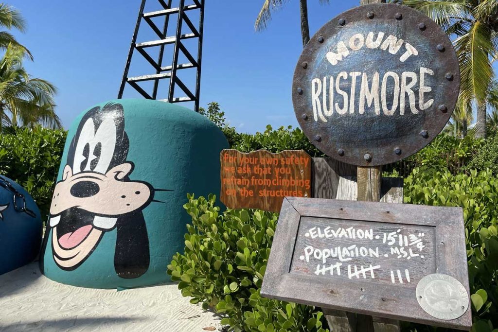 A large metal buoy, painted to resemble Goofy, near a sign reading Mount Rustmore