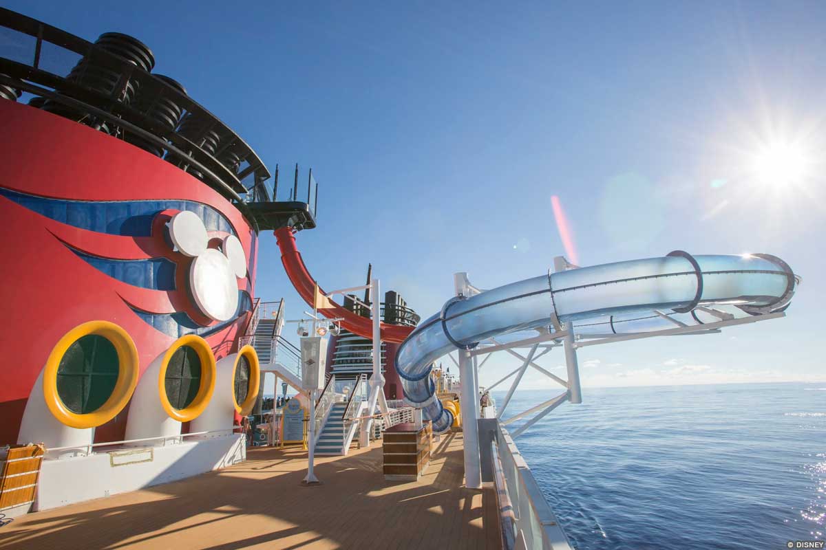 Image of the Aqua Dunk water slide, with a large clear tube coiled alongside the Disney Magic's distinctive red funnels (featuring a white Mickey Mouse silhouette and blue wave design)
