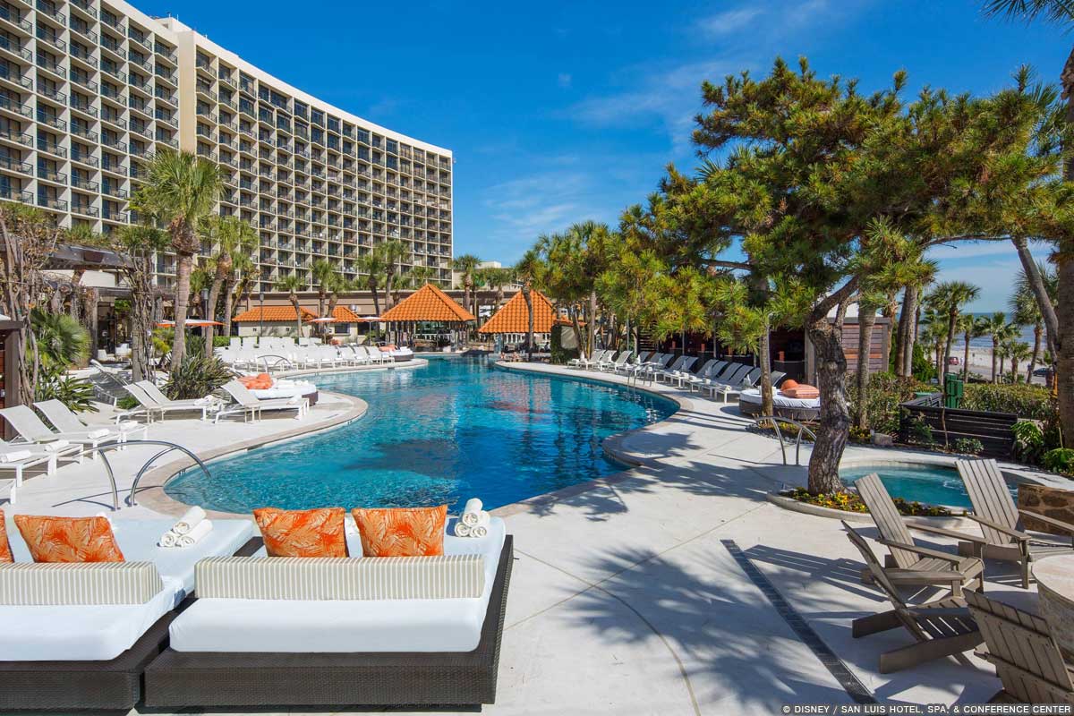 Exterior image of San Luis Hotel, with lounge chairs beside a pool and the Gulf of Mexico in the distance