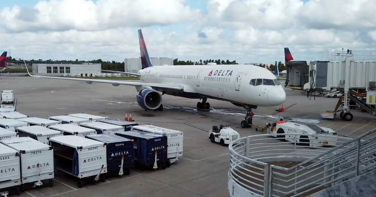 Image of a jet parked at an airport terminal, with service vehicles and luggage bins nearby