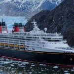A Disney Cruise Ship sails through icy waters, with mountains and an impressive glacier in the background