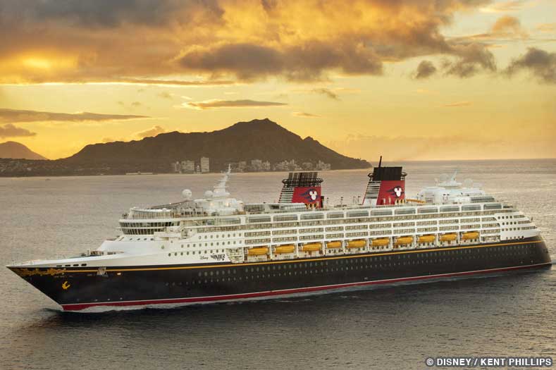 Disney Cruises to Hawaii - the Disney Wonder Cruise Ship sails along the ocean, with tall mountains in the background silhouetted by an orange sky at twilight | Image © Disney / Kent Phillips