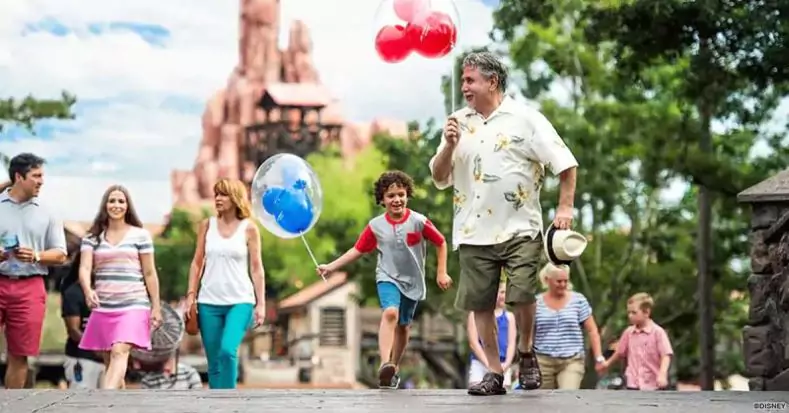 An older adult and younger child walk in Magic Kingdom, each holding Mickey-shaped balloons