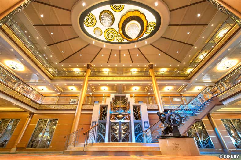 The lobby atrium of the Disney Magic, with a unique glass light fixture overhead and a statue of Mickey Mouse in the corner