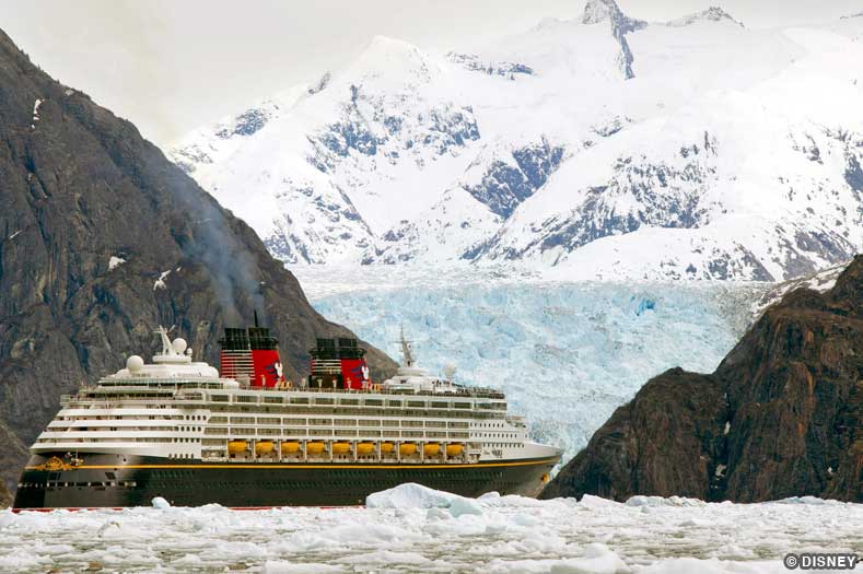 The Disney Wonder sails through an icy fjord toward a looming glacier in the shadow of steep mountainsides