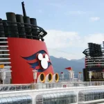 Cruising with Disney for the First Time -- Two red funnels atop a Disney Cruise Ship, each with a Mickey Mouse silhouette in white and a blue wave pattern