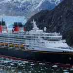 A Disney Cruise Ship sails through icy waters, with mountains and an impressive glacier in the background