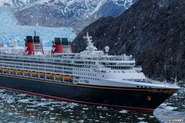 A Disney Cruise Ship sails through icy waters, with mountains and an impressive glacier in the background