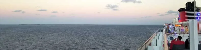 A wide-open view of the ocean, with the edge of the deck of a Disney Cruise Ship barely visible