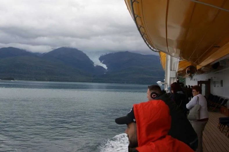 Passengers on a Disney Cruise to Alaska observe a distant glacier while sailing through a fjord