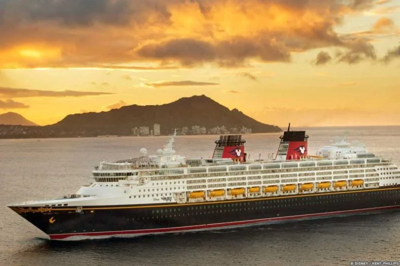 The Disney Wonder Cruise Ship sails in front of a Hawaiian mountain with an orange sky in the background