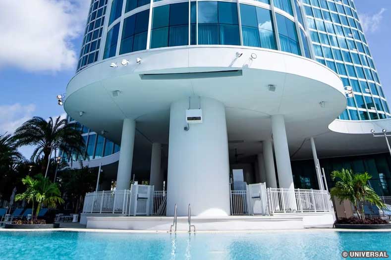 Exterior view of the gleaming glass tower of Aventura Hotel, with a crystal blue pool at the base