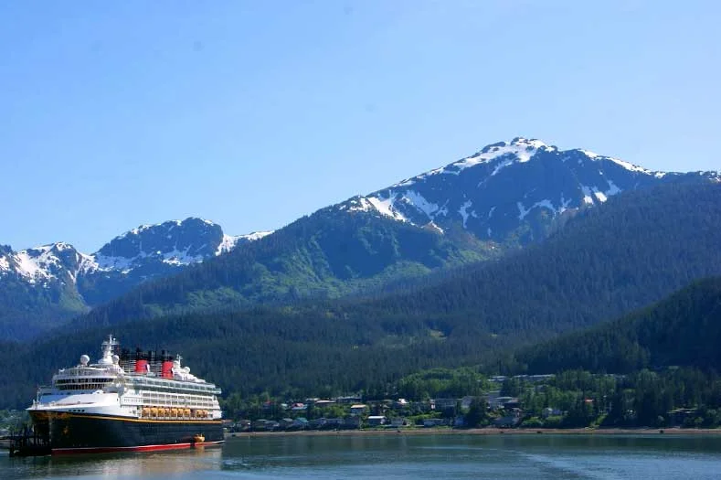 A Disney Cruise Ship docked in Alaska, with large snow-capped mountains in the background