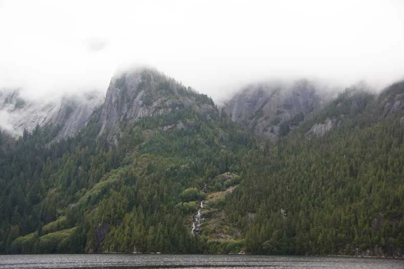 Misty mountaintops with waterfalls abutting a waterway