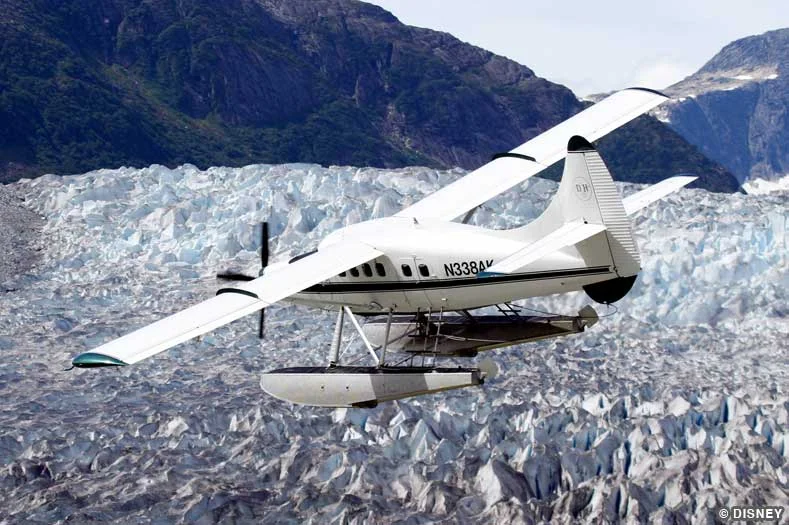 A white sea plane flies in front of a large craggy glacier