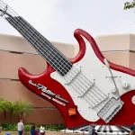 A giant red and white guitar-shaped marquee outside of Rock 'n' Roller Coaster. The bridge/neck of the guitar becomes a stylized roller coaster track.