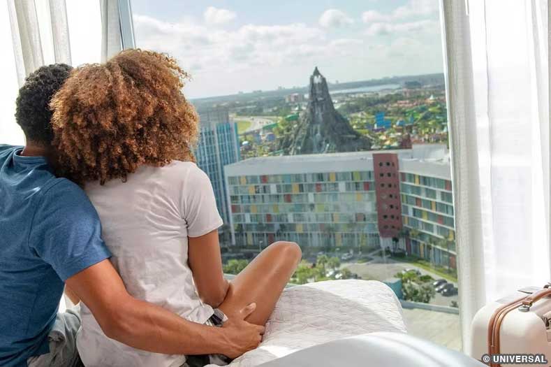 Two guests look out an upper floor window of Aventura Resorts toward the distant Volcano Bay water park