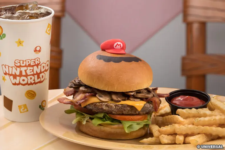 A beef patty, topped with mushrooms, lettuce, tomato, and American cheese, served on a brioche bun with a side of truffle French fries. The burger has a decorate mustache embossed on the bun's crown and is topped with a Mario hat